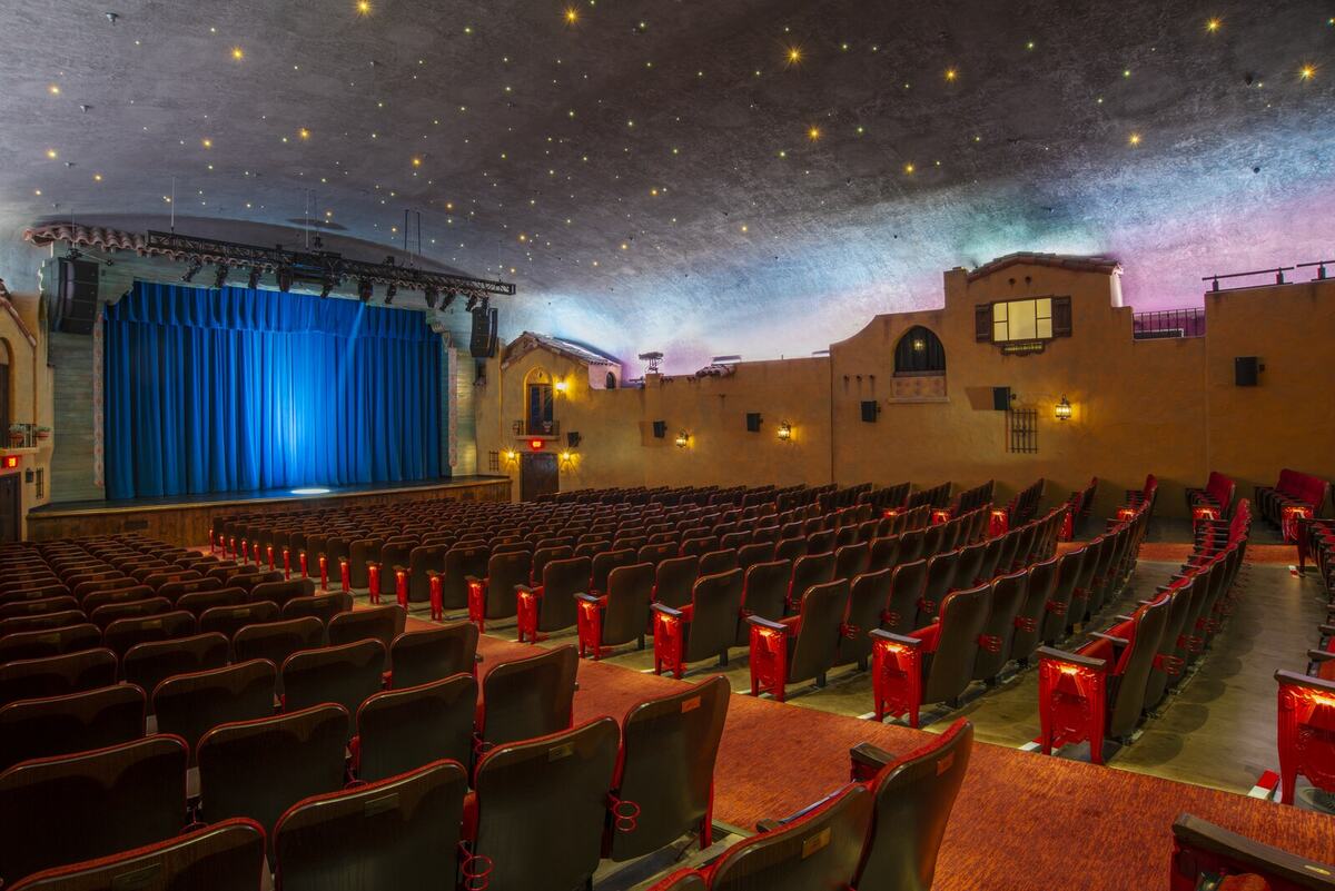 Restored Plaza Theatre auditorium showing period architecture, illuminated wall sconces, stage lighting, and star ceiling